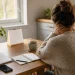 Femme assise près d'une fenêtre lumineuse, regard perdu dans le vide, tasse de thé entre les mains