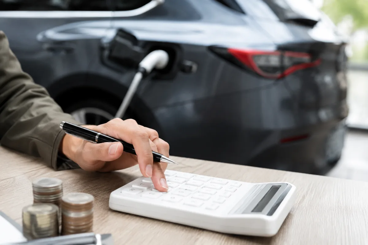 Main posant un câble de recharge sur la prise d'une voiture électrique blanche garée devant une maison